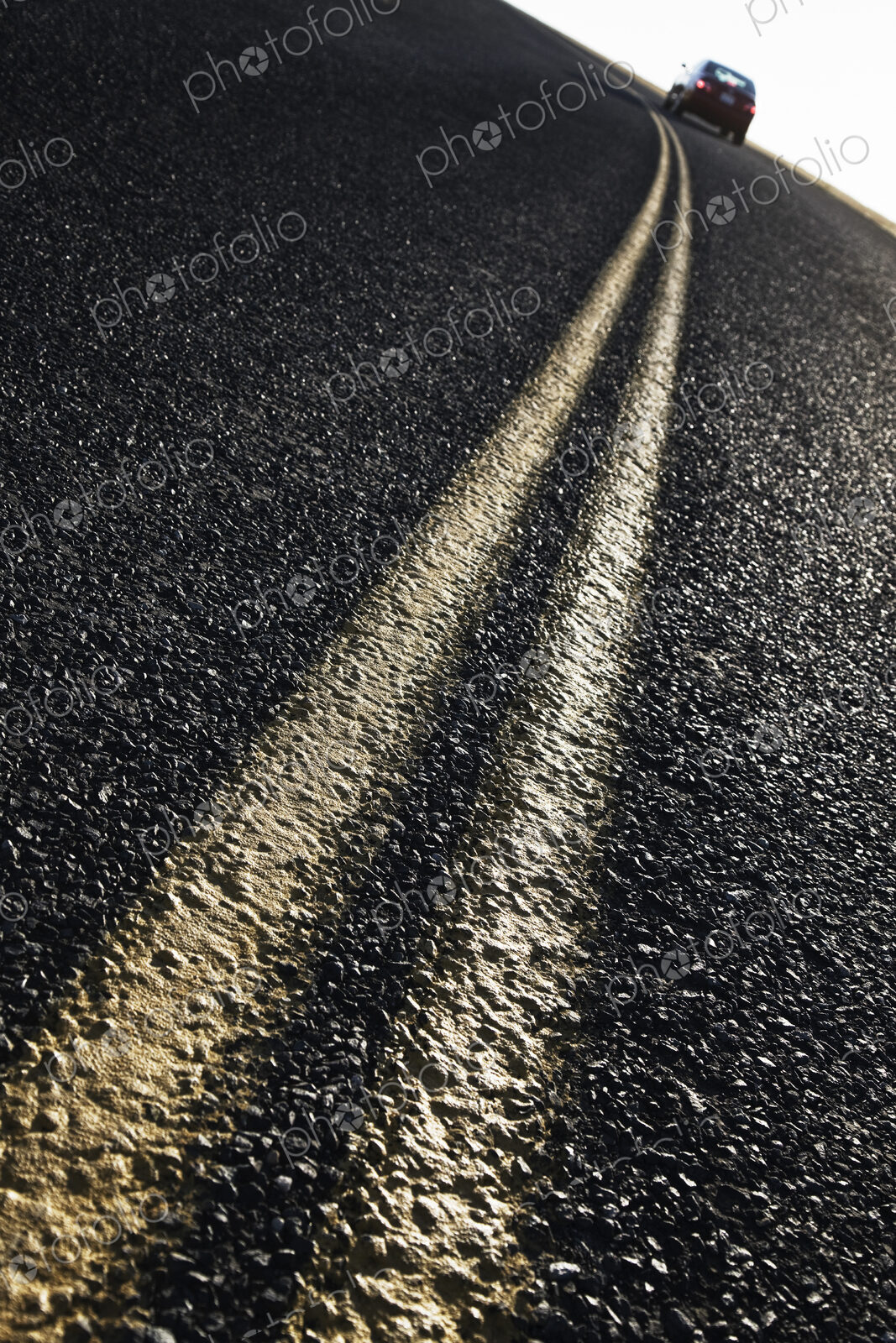Low angle view of a double line on a highway and a car in the background.