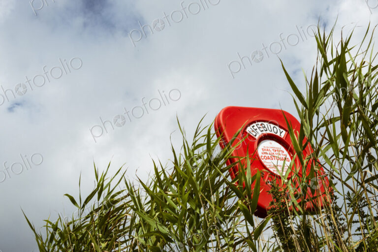 Low angle view of a red lifebuoy post and a sign, instructions to contact the…