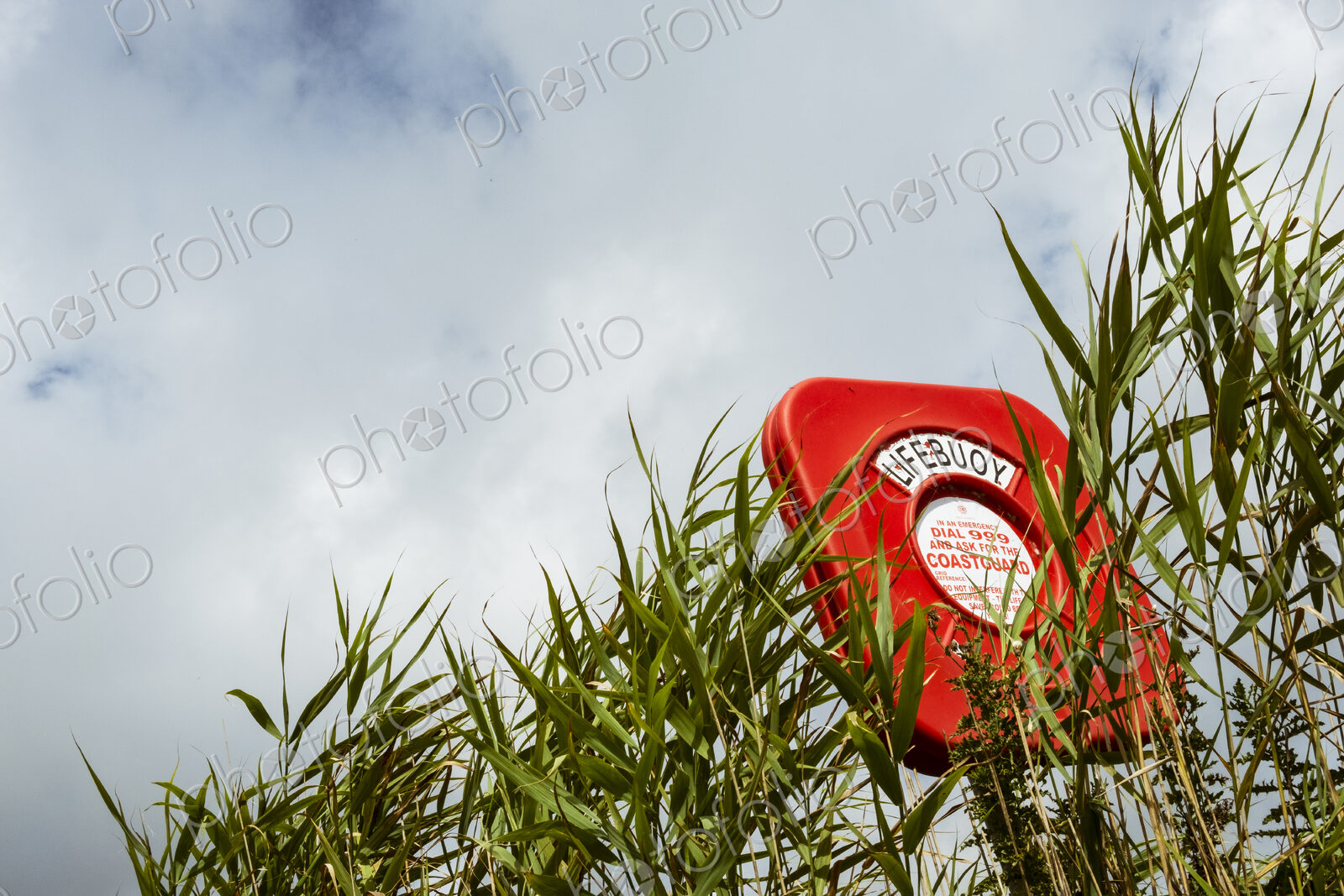 Low angle view of a red lifebuoy post and a sign, instructions to contact the…