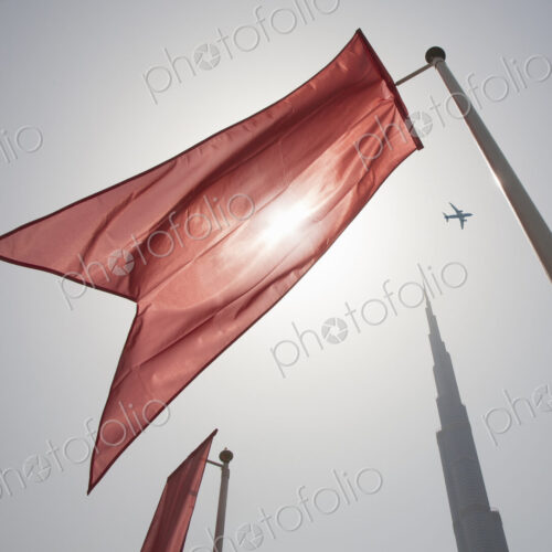 Low angle view of bright red flag on flagpoles fluttering in the wind, clear sky.