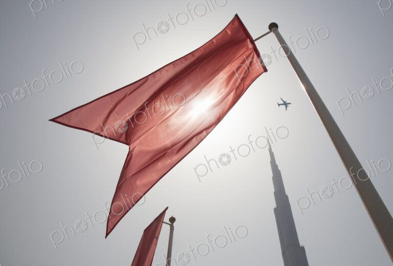 Low angle view of bright red flag on flagpoles fluttering in the wind, clear sky.