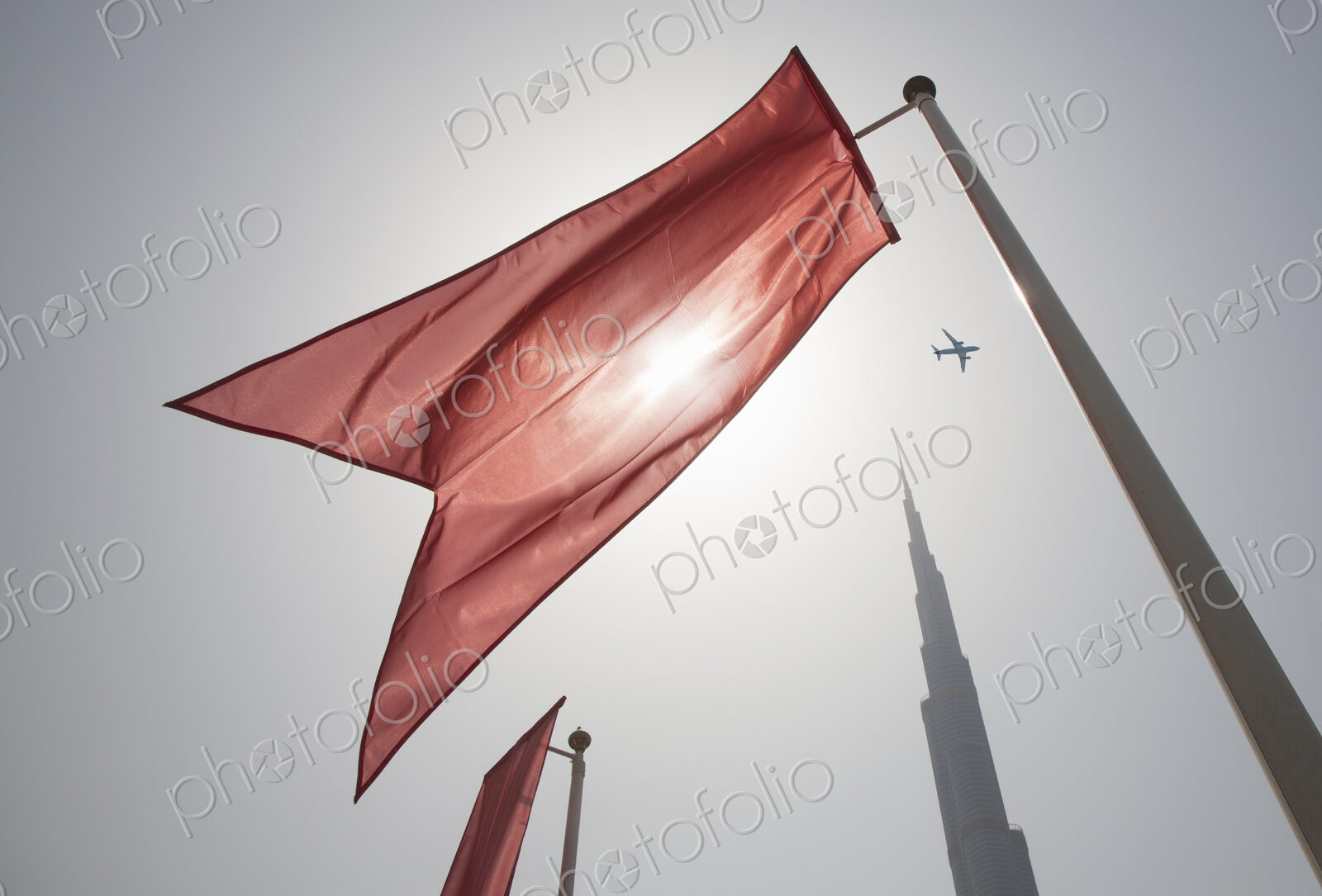 Low angle view of bright red flag on flagpoles fluttering in the wind, clear sky.