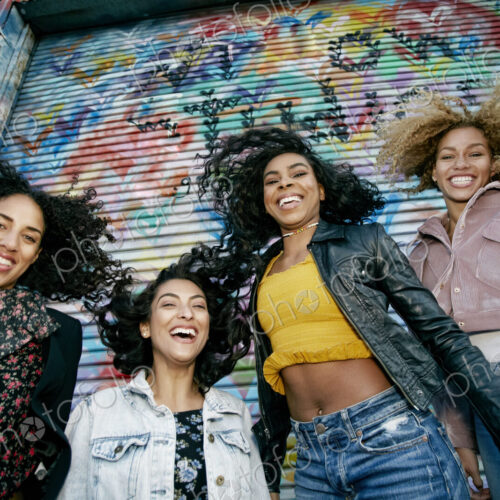 Low angle view of four young women with curly hair standing in front of shutter… Low angle view of four young women with curly hair standing in front of shutter…