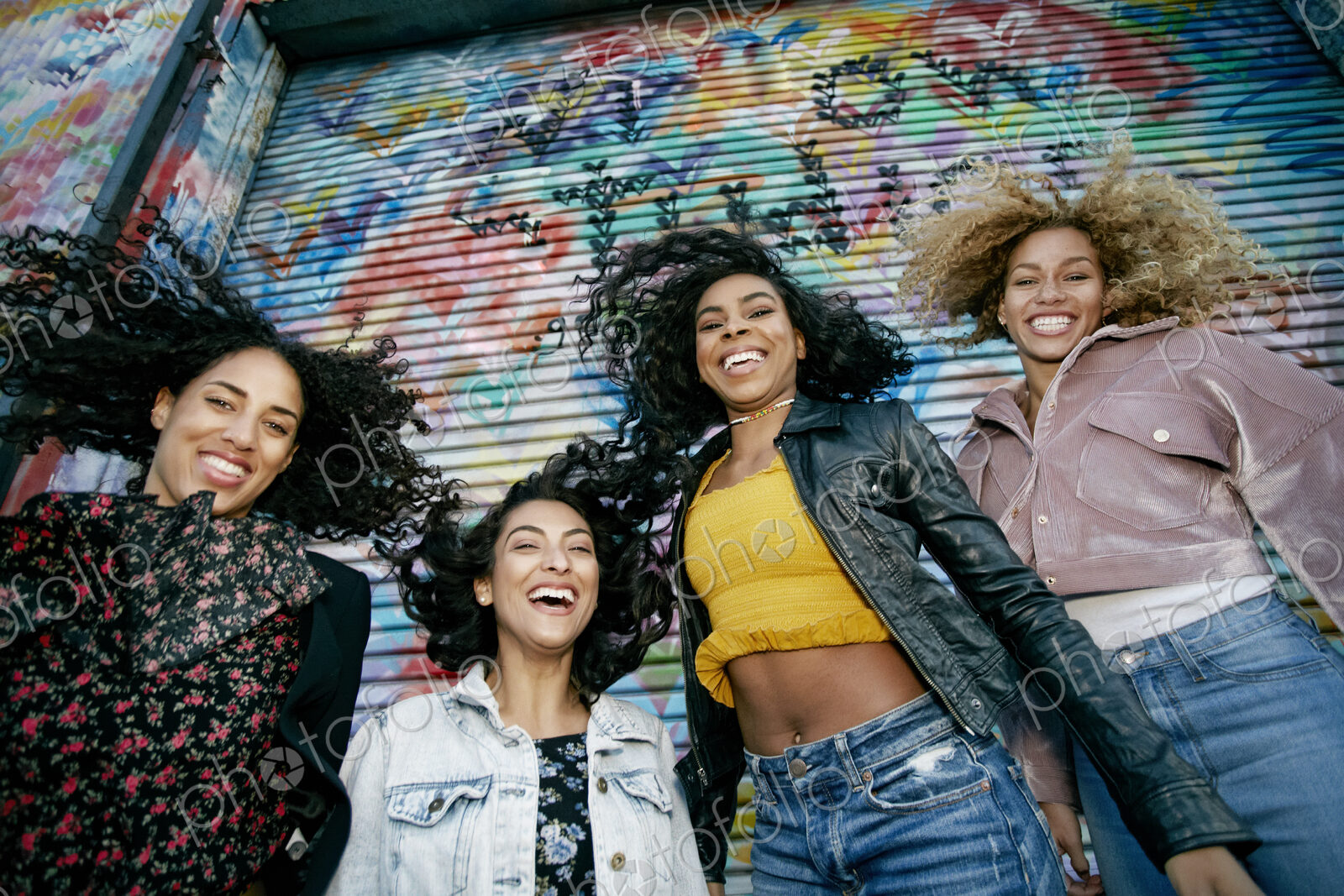 Low angle view of four young women with curly hair standing in front of shutter…