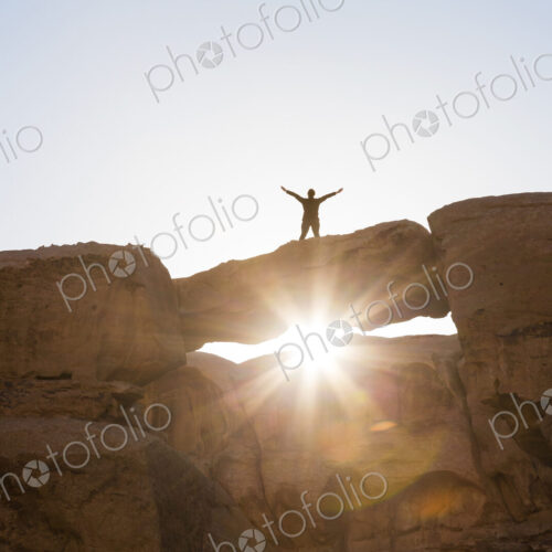 Low angle view of woman standing with her arms outstretched on a natural rock bridge… Low angle view of woman standing with her arms outstretched on a natural rock bridge…