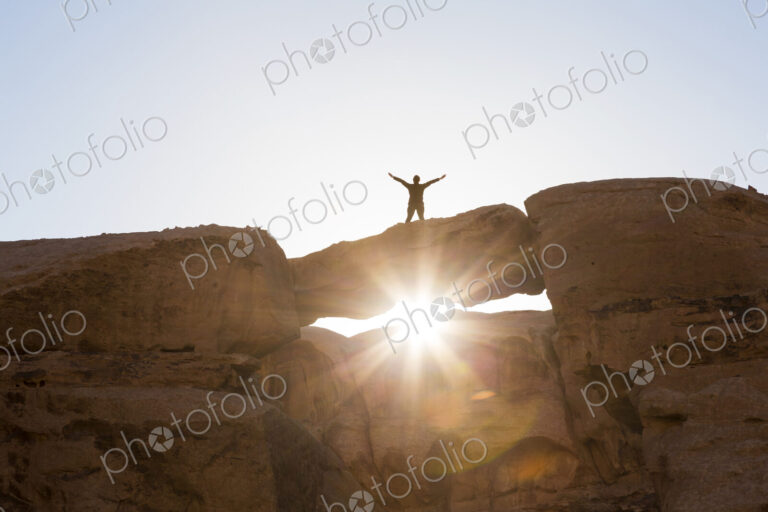 Low angle view of woman standing with her arms outstretched on a natural rock bridge…