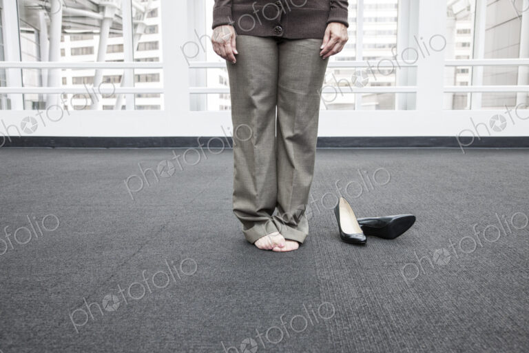 Low closeup view of a businesswoman standing on a carpet in bare feet.