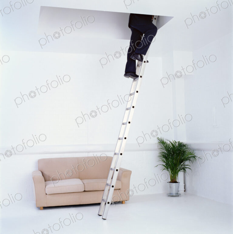 Low section of businessman wearing dark suit climbing up a ladder into a ceiling hatch.