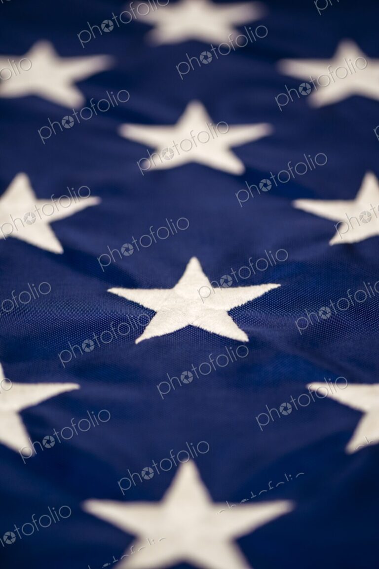 Macro detail of multiple white embroidered stars on the blue field of the American…