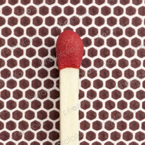 Macro photo of a single red-tipped wooden matchstick resting on the brown textured…