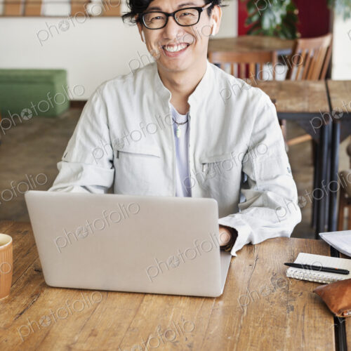 Male Japanese professional sitting at a table in a co-working space, using laptop…