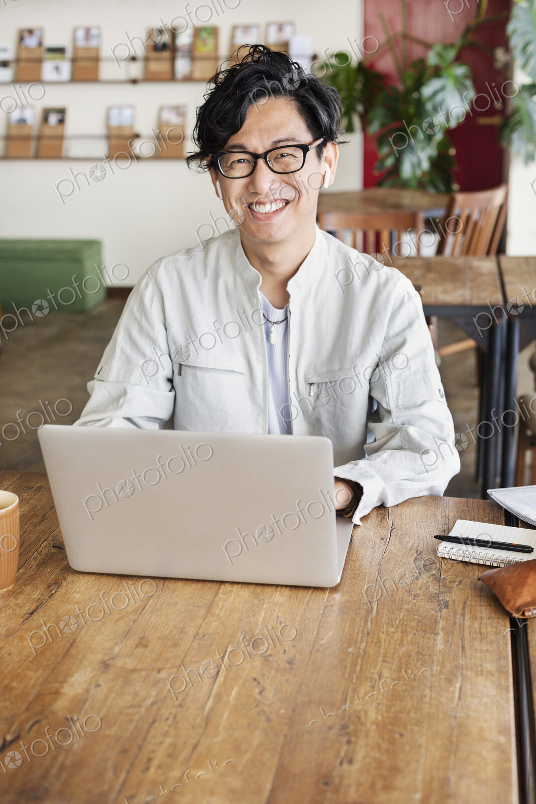 Male Japanese professional sitting at a table in a co-working space, using laptop…