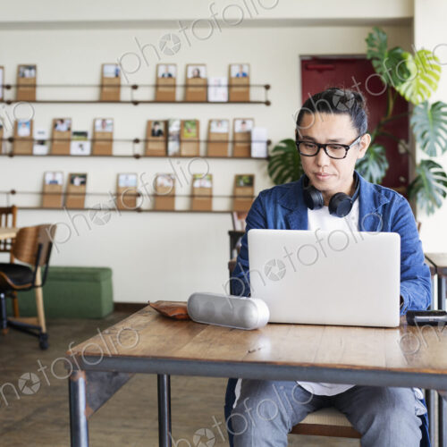 Male Japanese professional sitting at a table in a co-working space, using laptop…
