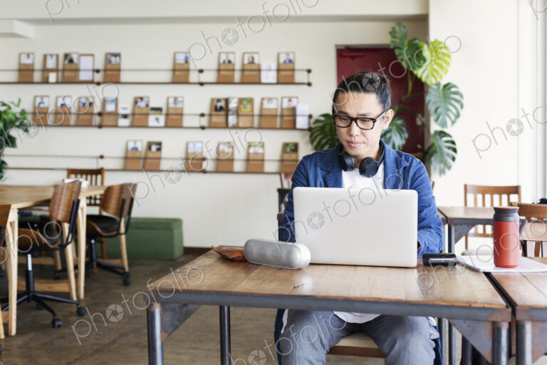 Male Japanese professional sitting at a table in a co-working space, using laptop…