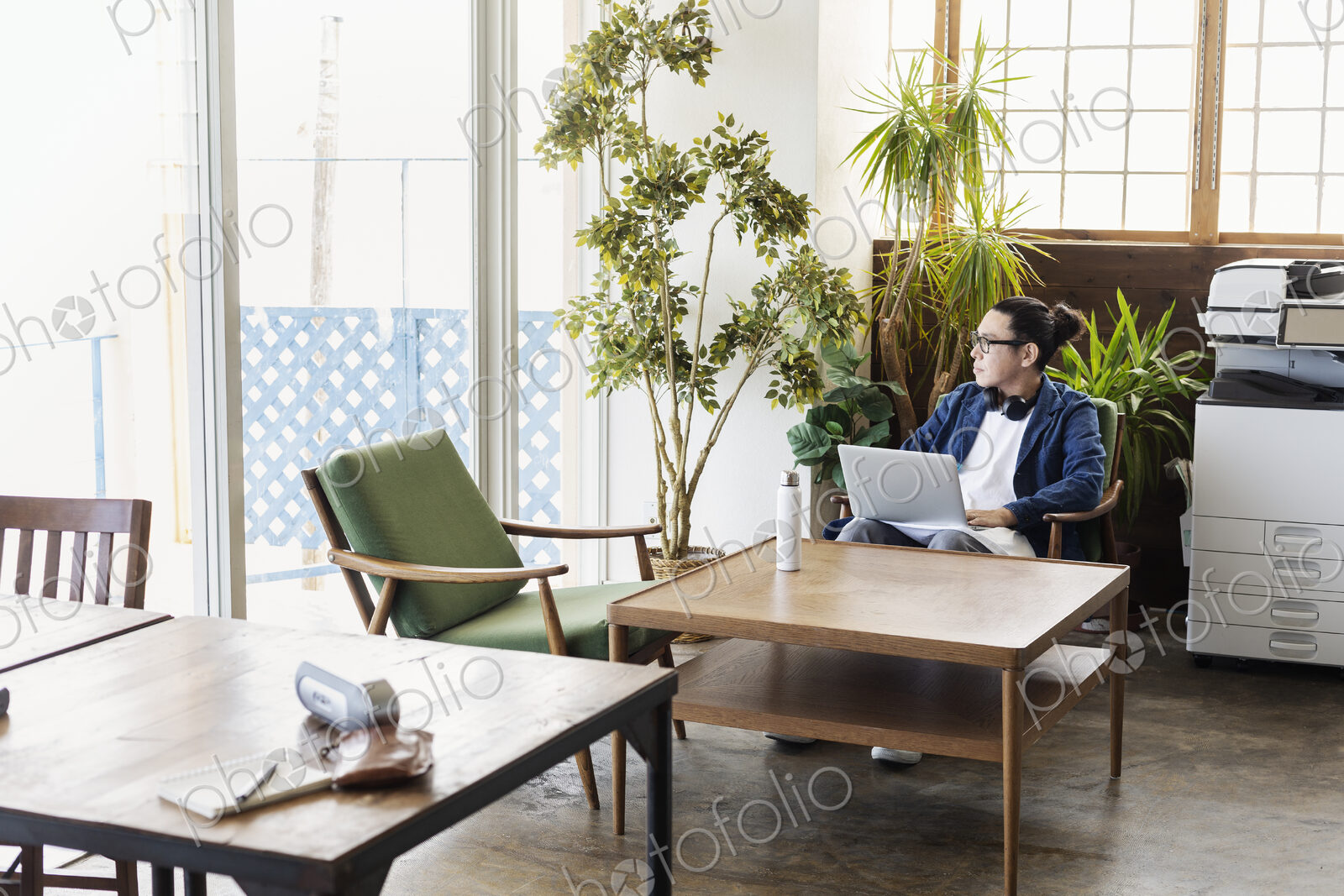 Male Japanese professional sitting at a table in a co-working space, using laptop…