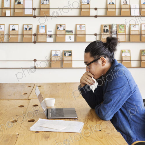 Male Japanese professional sitting at a table in a co-working space, using laptop…
