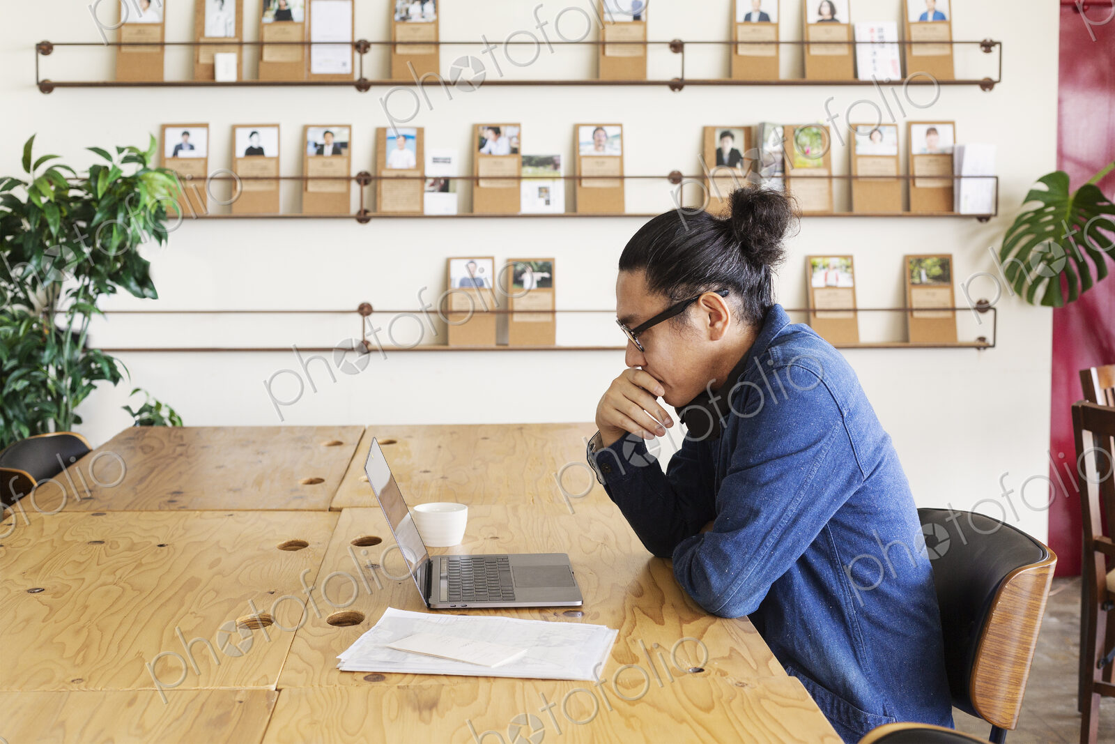 Male Japanese professional sitting at a table in a co-working space, using laptop…