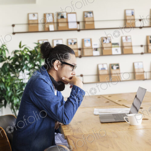 Male Japanese professional sitting at a table in a co-working space, using laptop…