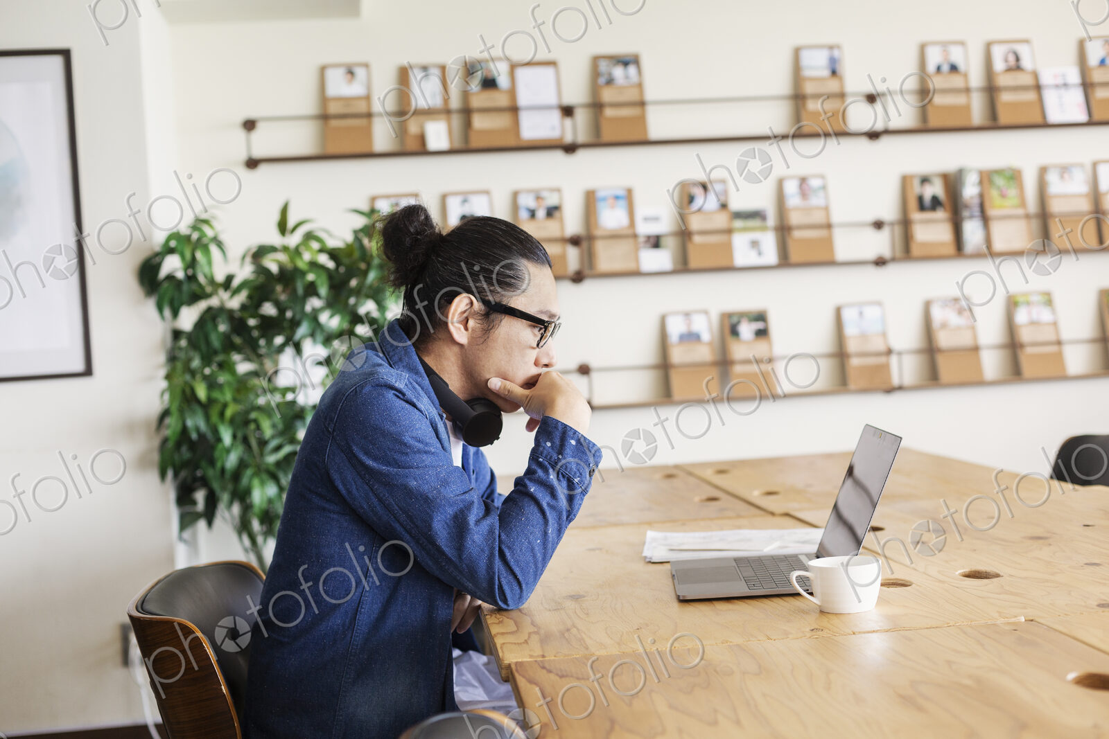 Male Japanese professional sitting at a table in a co-working space, using laptop…