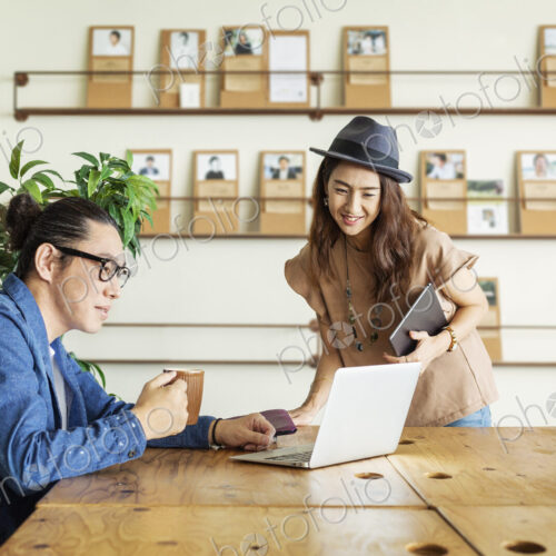 Male and female Japanese professional at a table in a co-working space, using laptop… Male and female Japanese professional at a table in a co-working space, using laptop…