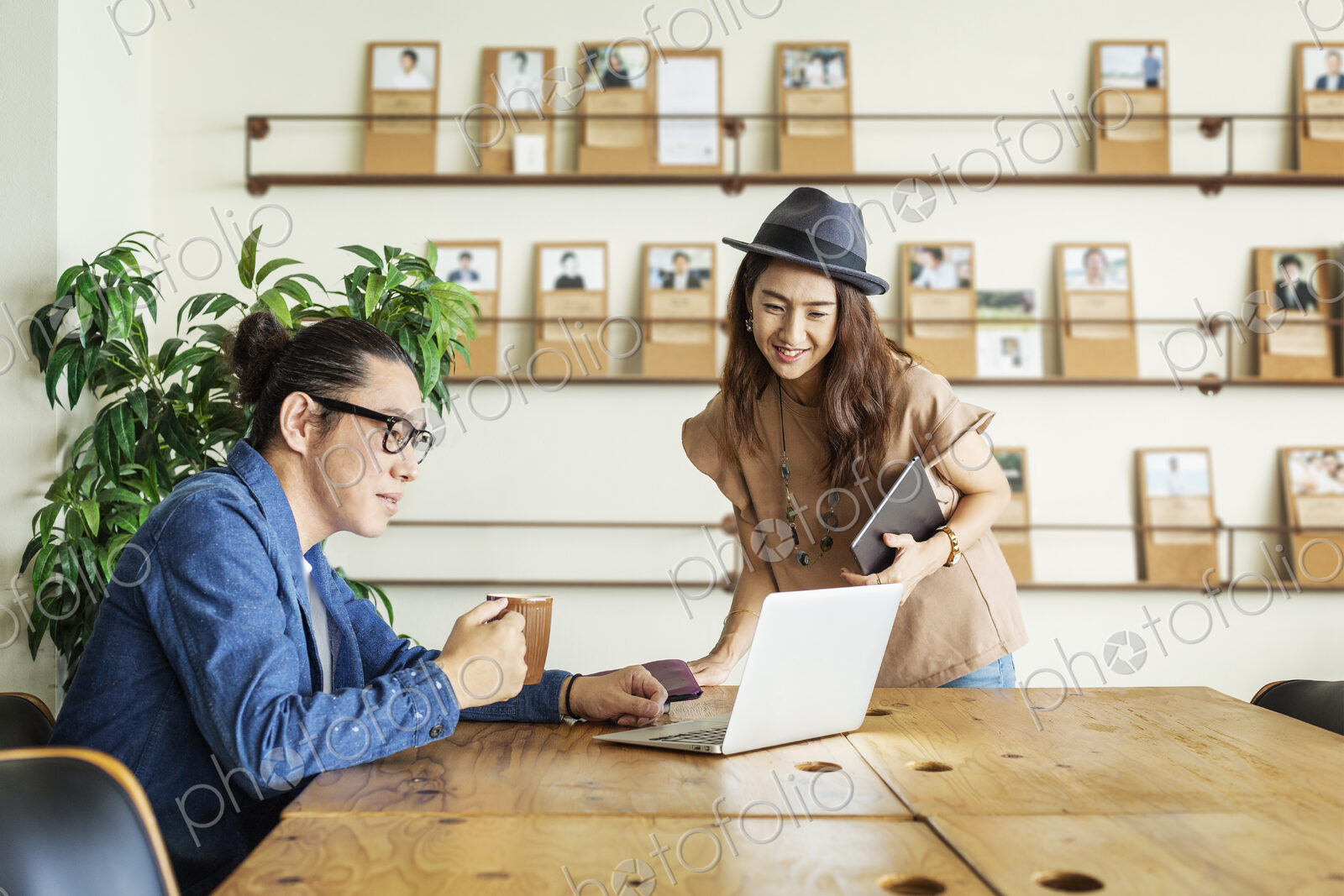 Male and female Japanese professional at a table in a co-working space, using laptop…