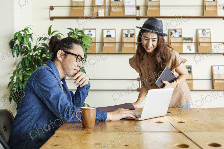 Male and female Japanese professional at a table in a co-working space, using laptop…