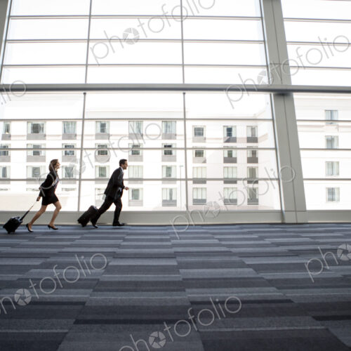 Male and female business people running past a window in the lobby of a conference centre Male and female business people running past a window in the lobby of a conference centre
