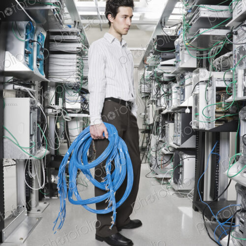 Male computer technician holding CAT 5 cables and standing in the aisle of a computer… Male computer technician holding CAT 5 cables and standing in the aisle of a computer…