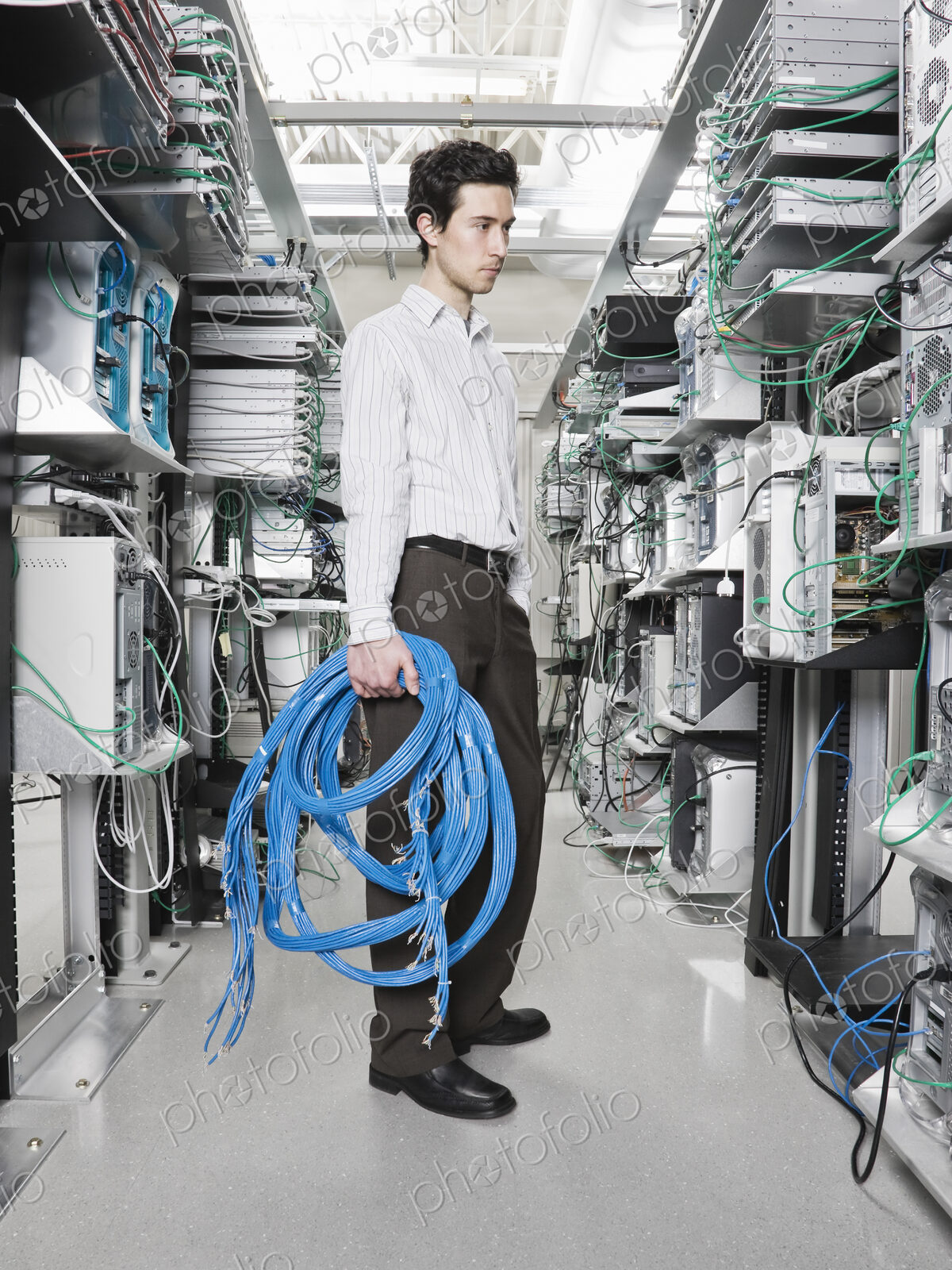 Male computer technician holding CAT 5 cables and standing in the aisle of a computer…