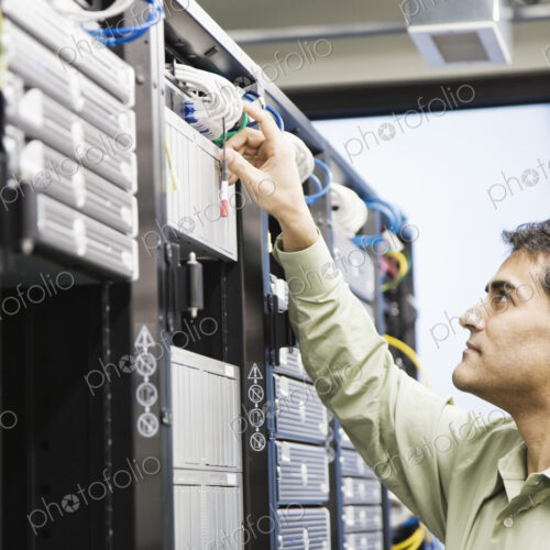 Male computer technician working on servers in a computer server farm. Male computer technician working on servers in a computer server farm.