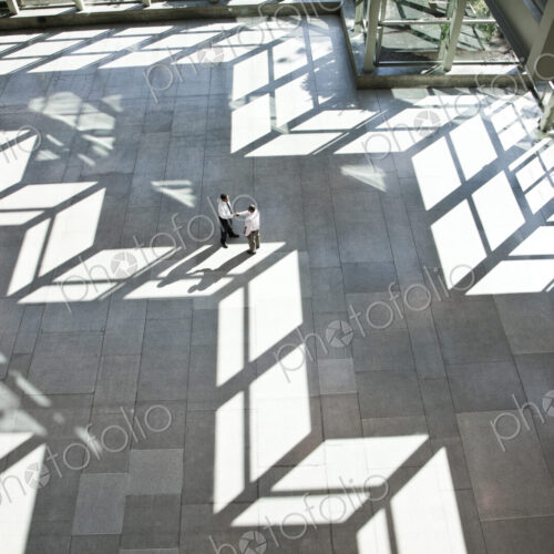 Male doctors conferring over medical records in a hospital lobby. Male doctors conferring over medical records in a hospital lobby.