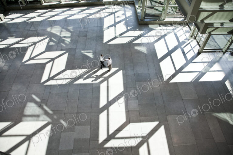 Male doctors conferring over medical records in a hospital lobby.