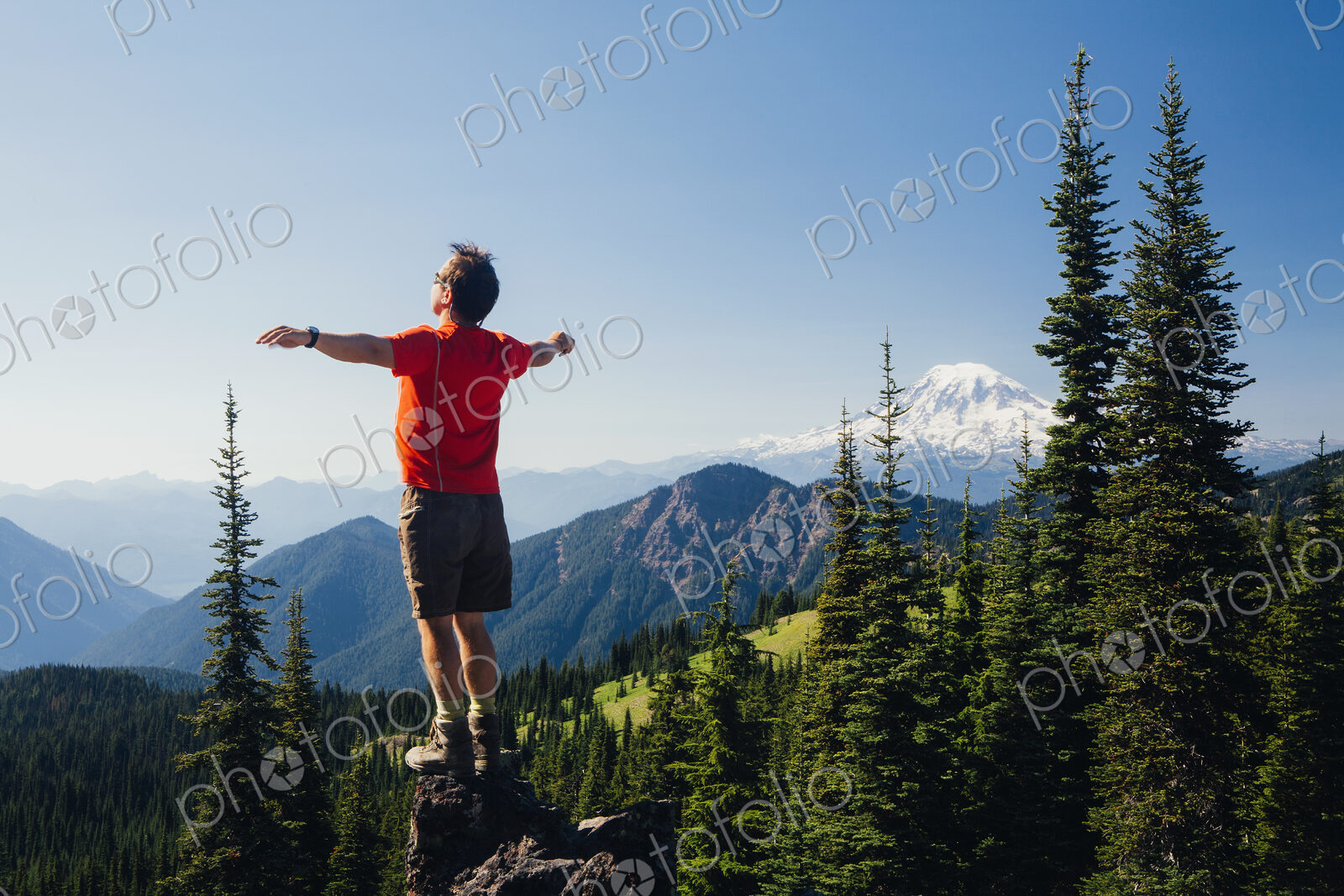 Male hiker standing with his arms outstretched on a mountain top, looking over the…
