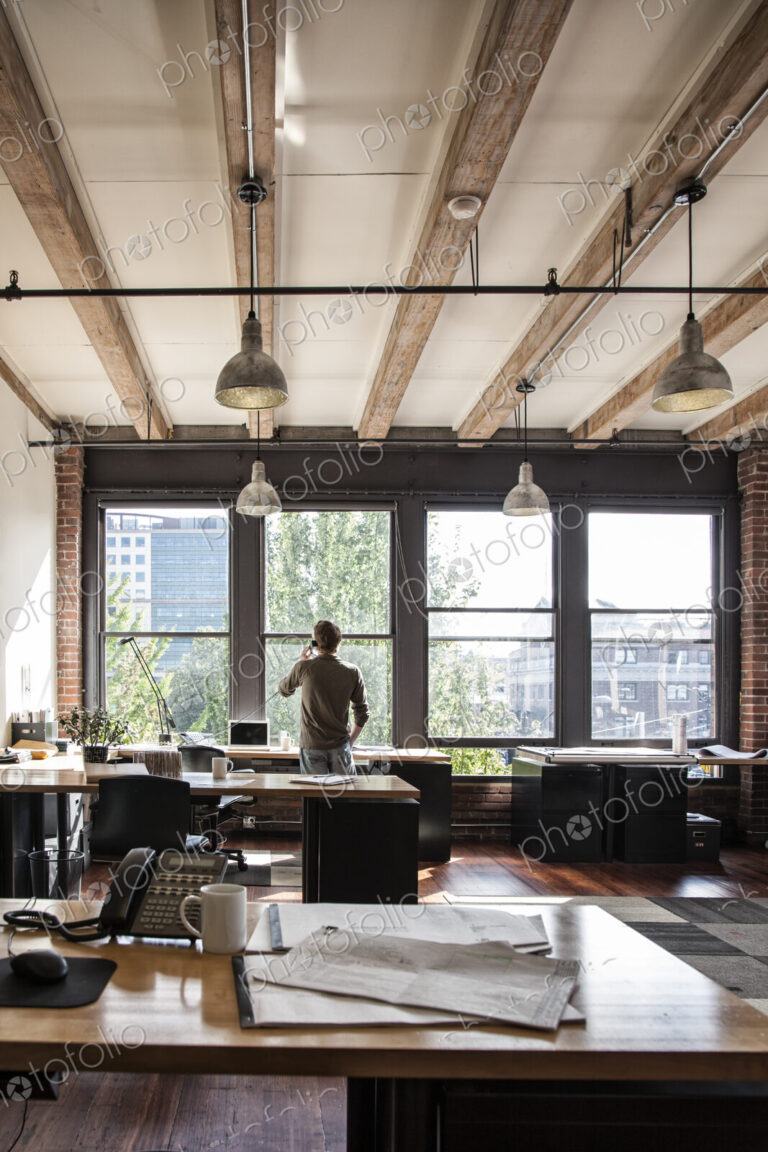 Male office worker on phone looking out windows of a creative office.