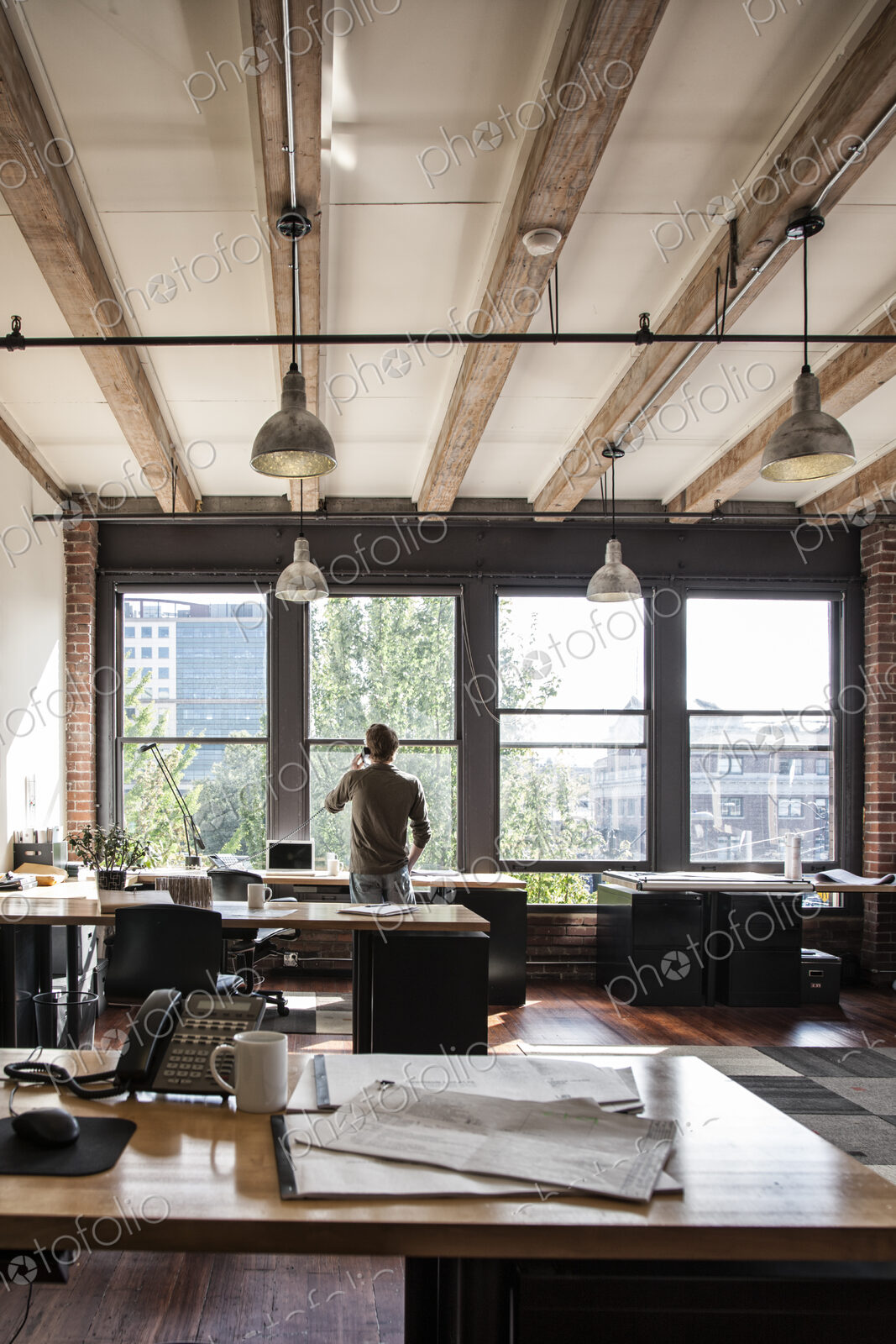Male office worker on phone looking out windows of a creative office.