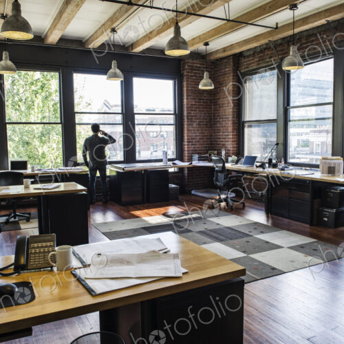 Male office worker on phone looking out windows of a creative office.