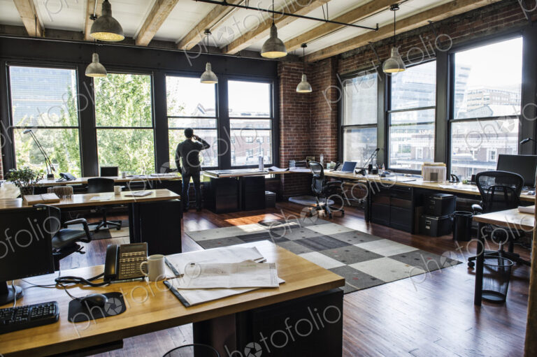 Male office worker on phone looking out windows of a creative office.