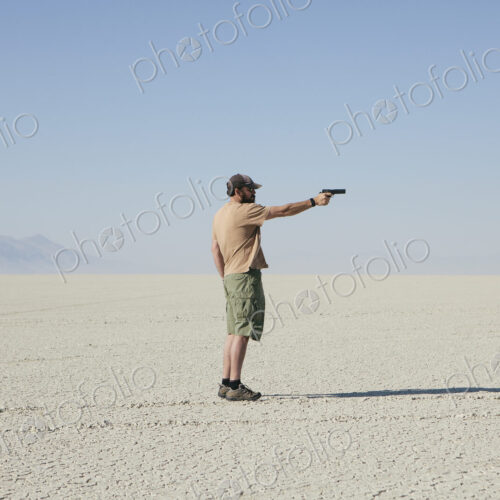 Man aiming hand gun, standing in vast, barren desert Man aiming hand gun, standing in vast, barren desert