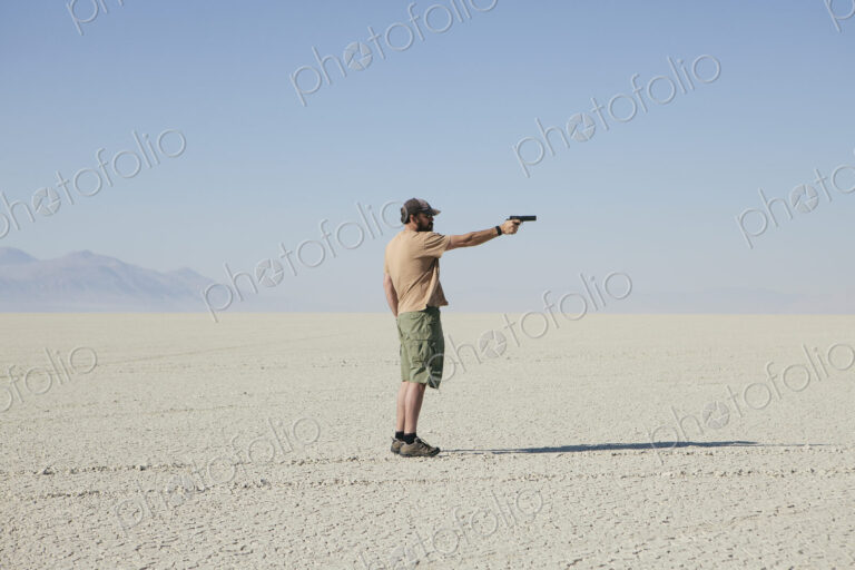 Man aiming hand gun, standing in vast, barren desert
