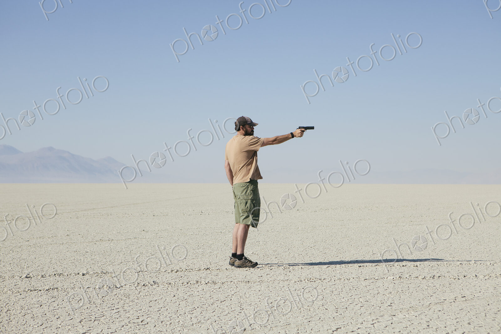 Man aiming hand gun, standing in vast, barren desert