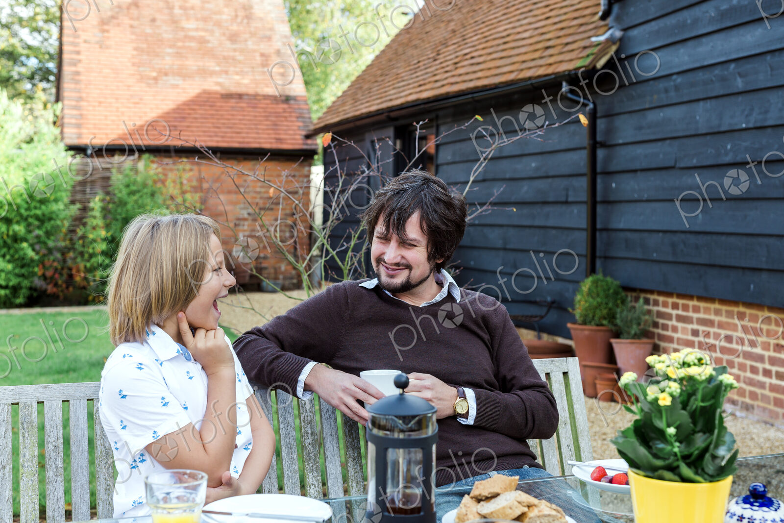 Man and boy having breakfast together at bench outside rural house.