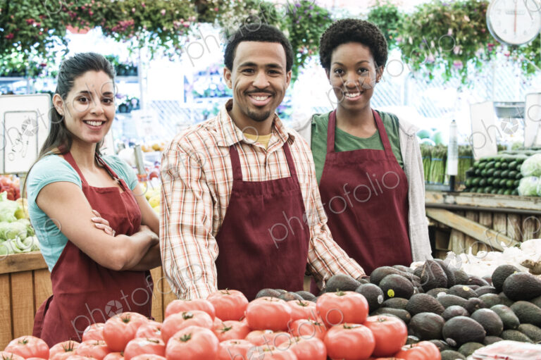 Man and two women wearing aprons standing at stall with fresh tomatoes at a fruit and…