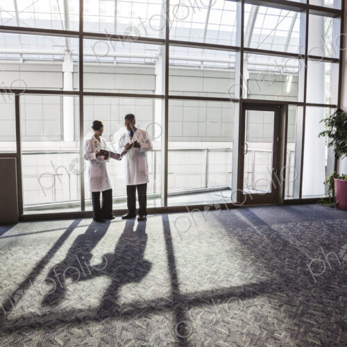 Man and woman doctors conferring over medical records in a hospital lobby. Man and woman doctors conferring over medical records in a hospital lobby.