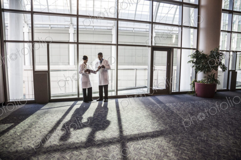 Man and woman doctors conferring over medical records in a hospital lobby.