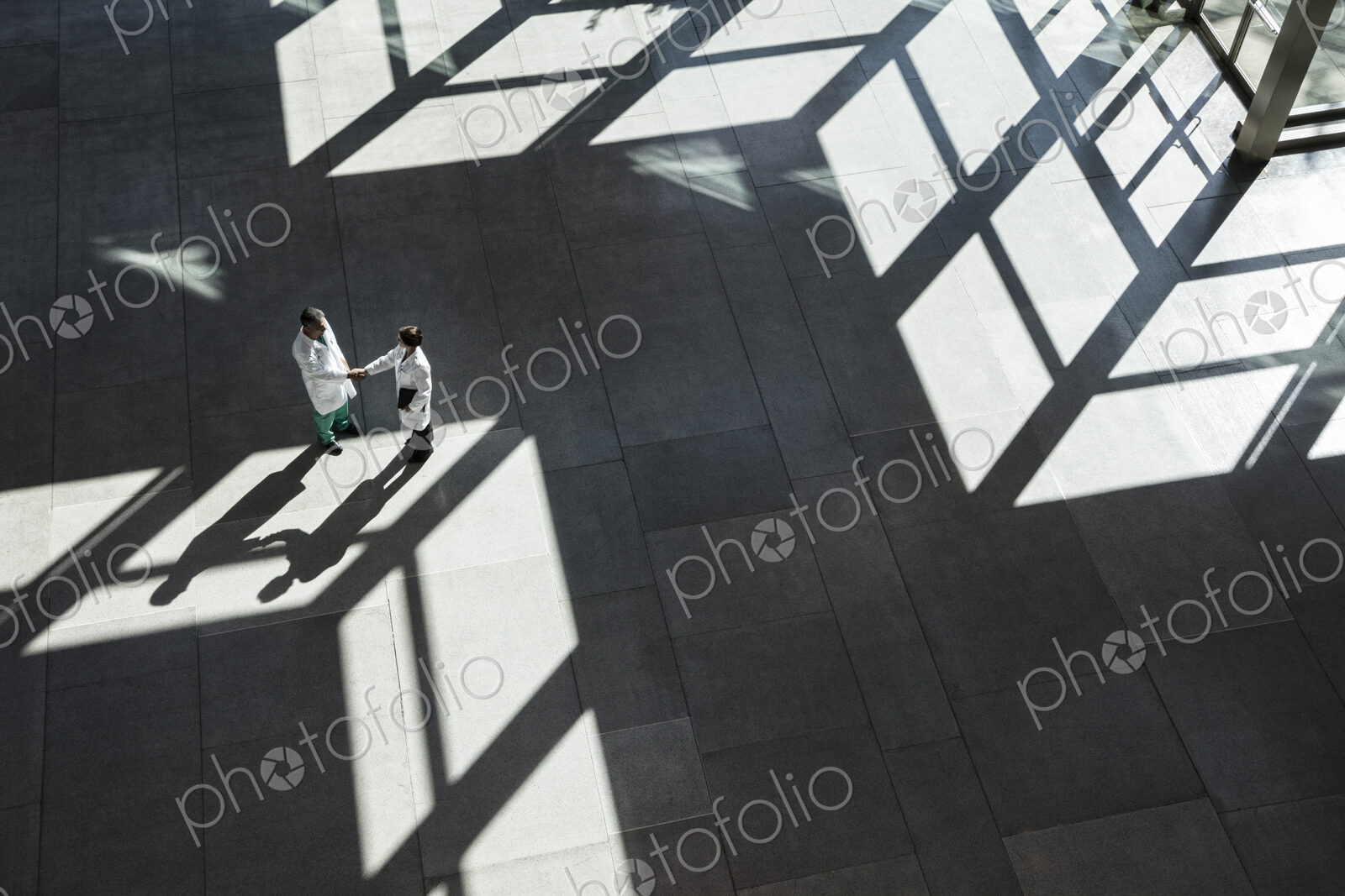 Man and woman doctors conferring over medical records in a hospital lobby.