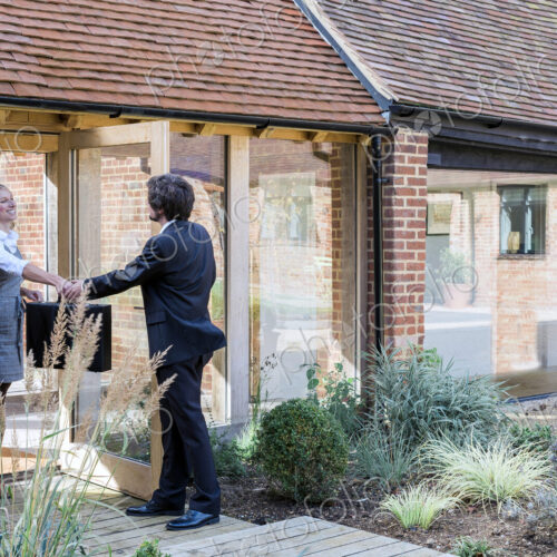 Man and woman handing over briefcase at door of barn conversion house. Man and woman handing over briefcase at door of barn conversion house.