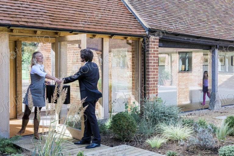 Man and woman handing over briefcase at door of barn conversion house.