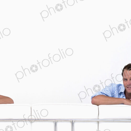 Man and woman looking over the back of a sofa at camera with white background. Man and woman looking over the back of a sofa at camera with white background.