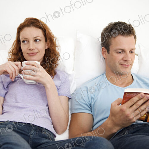 Man and woman relaxing together, woman with a mug, man reading a book.