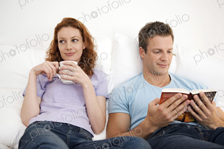 Man and woman relaxing together, woman with a mug, man reading a book.
